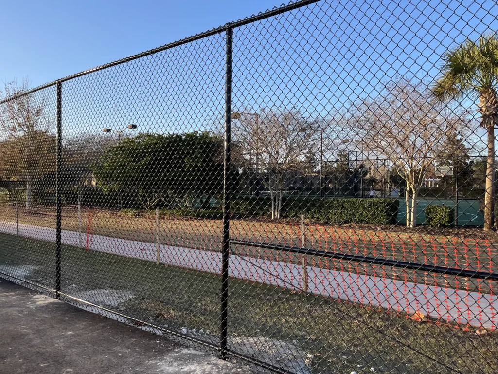 Tall black chain link fence around tennis and basketball courts at a recreation park