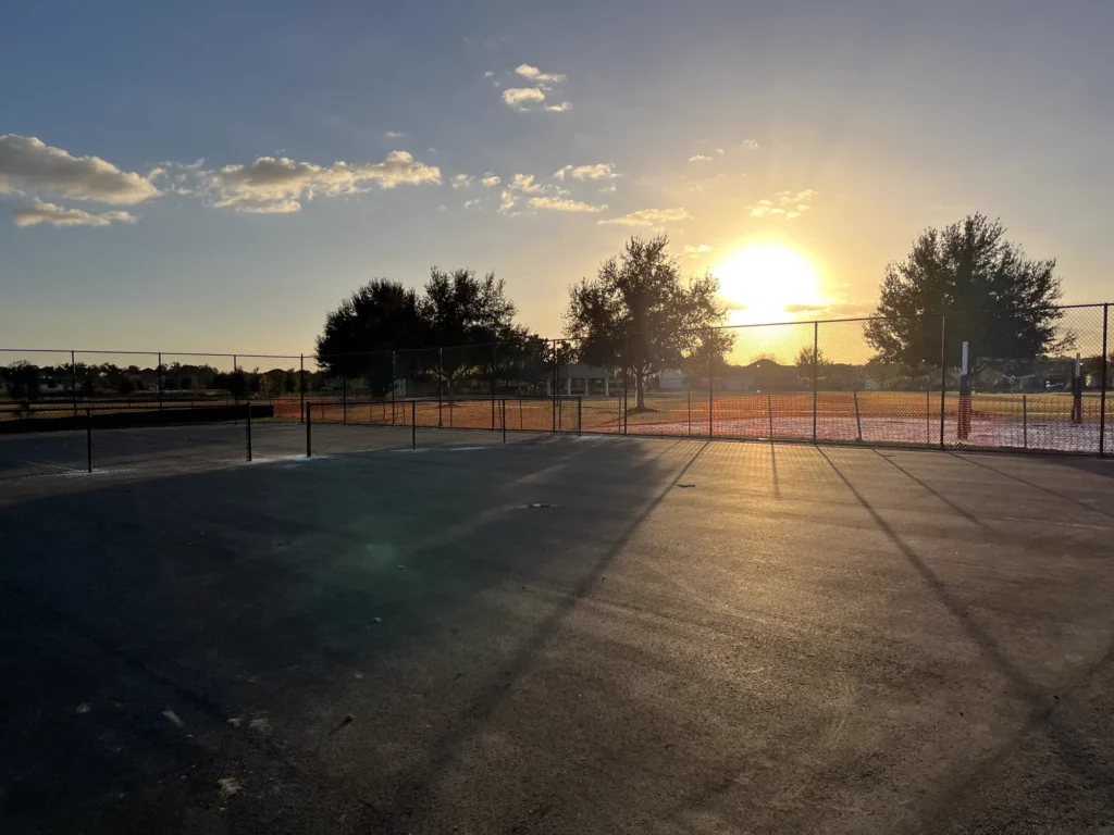 Sunset over a new black chain link court enclosure at a Florida sports complex