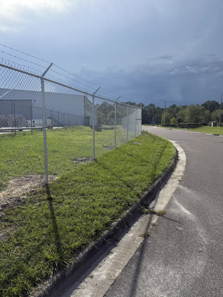 Galvanized chain link security fence with barbed wire along an industrial access road