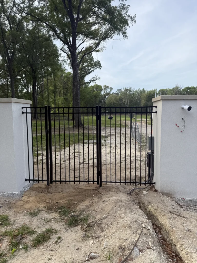 Black aluminum driveway gate with automatic opener between stucco entry columns