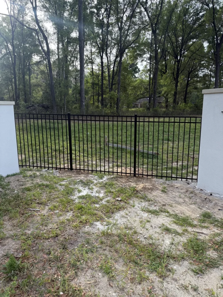 Black aluminum fence panel set between stucco columns at a rural property