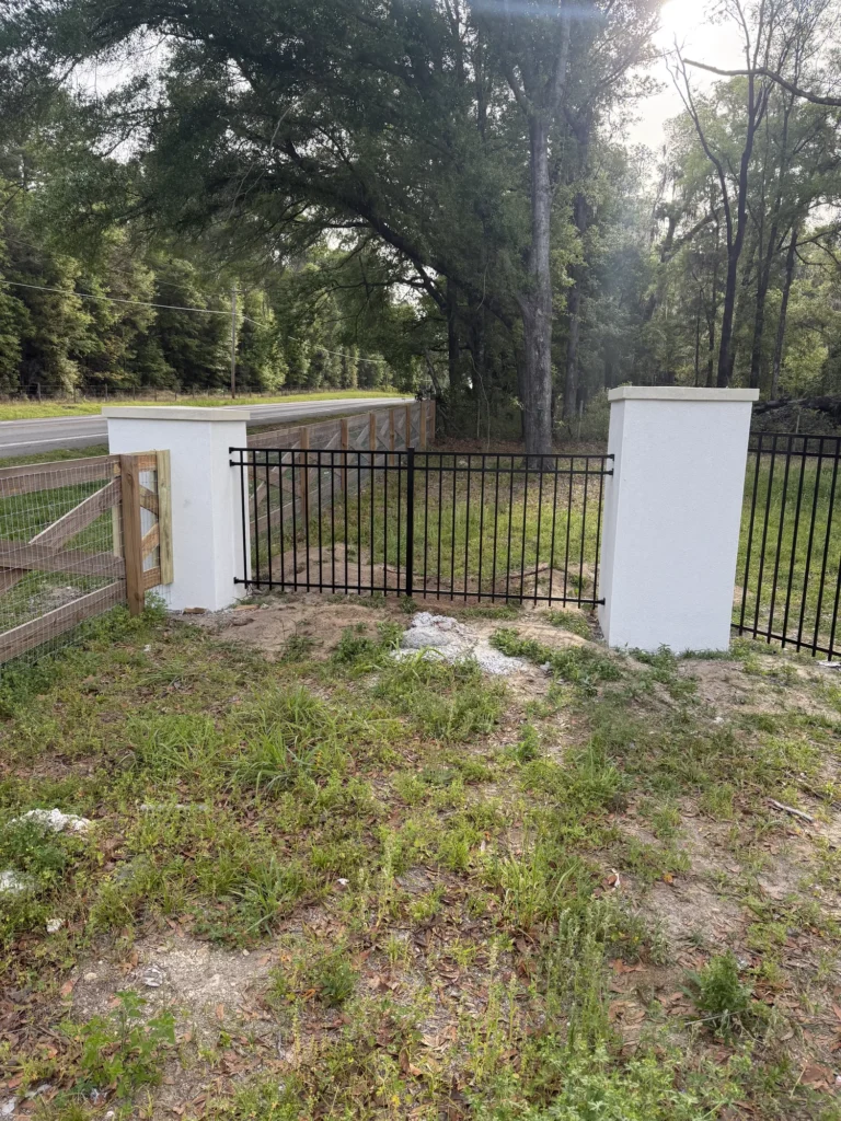 Black aluminum estate fence meeting the road at a rural property entrance