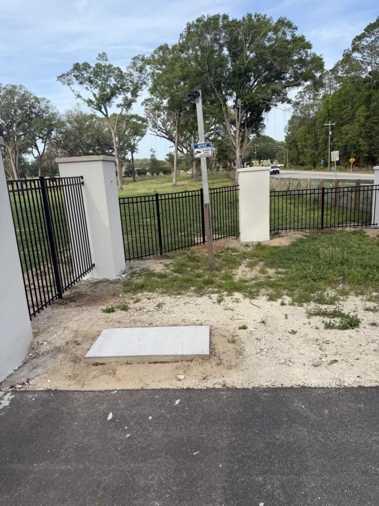 Stucco entry column and black aluminum fence along a country road