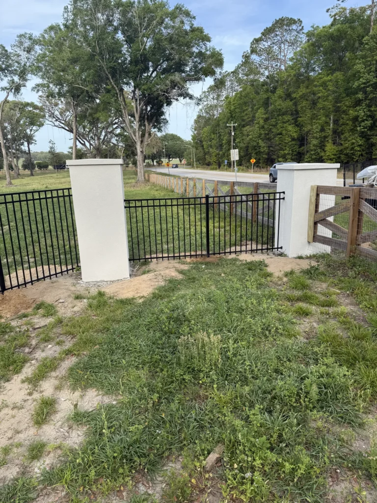 Black aluminum fence and stucco columns along a rural roadside
