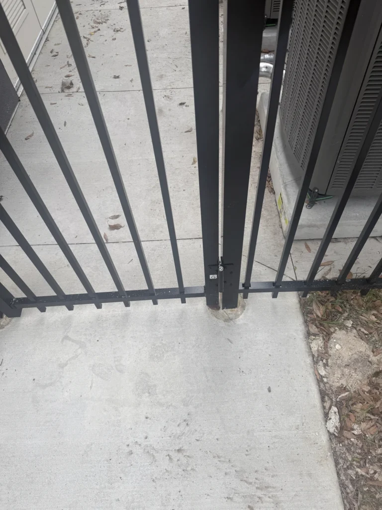 Self-closing gate latch on a black aluminum equipment enclosure
