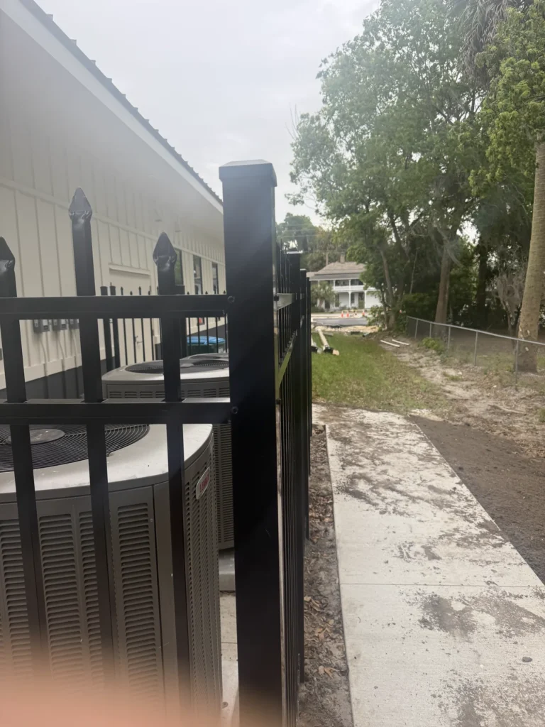 Black aluminum spear-top fence enclosing HVAC units at a commercial building