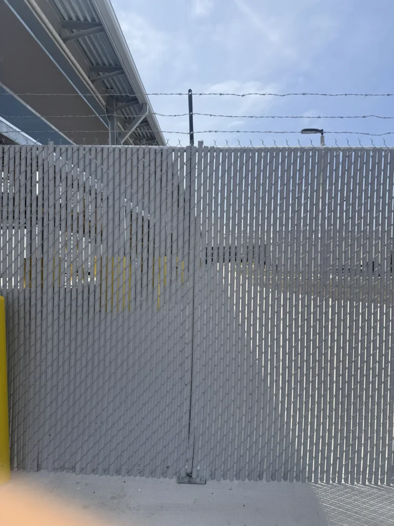Privacy slat chain link fence topped with barbed wire at a commercial site