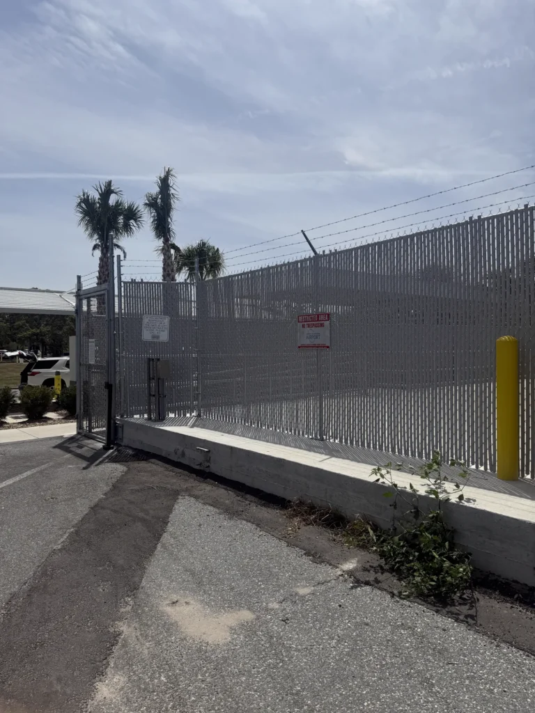 Rolling chain link gate with privacy slats and barbed wire at a commercial entrance
